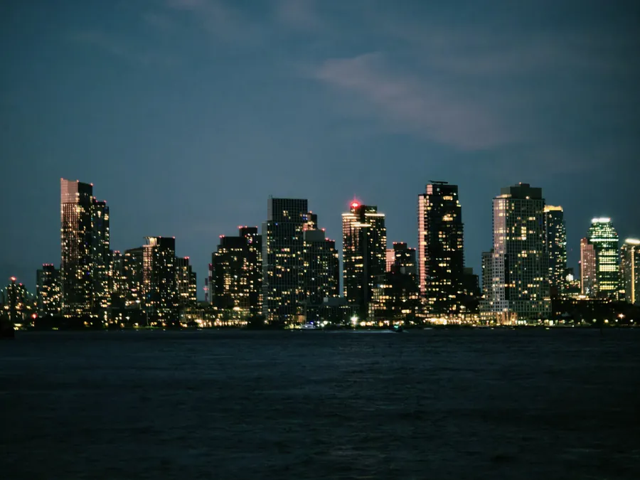 New York City skyline glowing across the river after dark